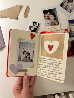 a hand holding an open book with pictures and hearts on the pages in front of it