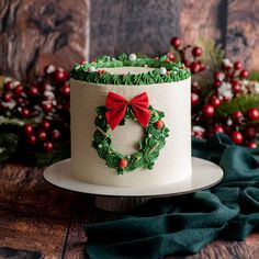 a decorated christmas cake sitting on top of a wooden table next to holly wreaths