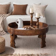 a coffee table with candles on it in front of a white couch and throw pillows