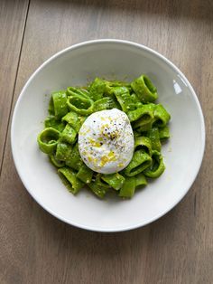 a white bowl filled with green food on top of a wooden table