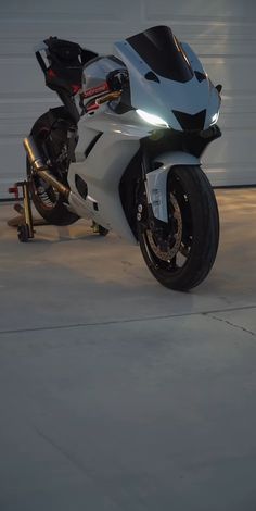 a white and black motorcycle parked in front of a garage door with tools on the ground