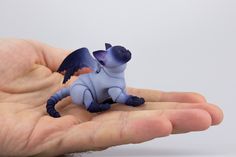 a small toy dragon sitting on the palm of someone's hand in front of white background