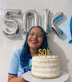 a woman holding a cake with the number fifty six on it in front of balloons