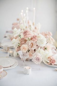 the table is set with white and pink flowers, candles, and plates on it