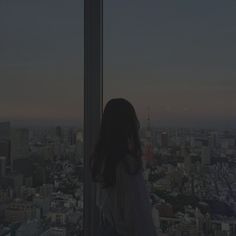 a woman standing in front of a window looking out at the cityscape and skyscrapers