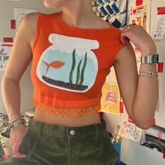 a woman wearing an orange crop top with a fish in a bowl on it's chest