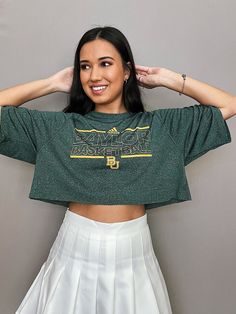 a woman in a green shirt and white skirt posing for the camera with her hands on her head