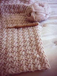 a crocheted blanket and ball of yarn sitting on a bed next to each other