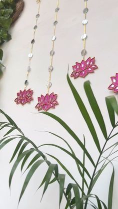 three pink flowers are hanging on a white wall next to a green plant and some beads