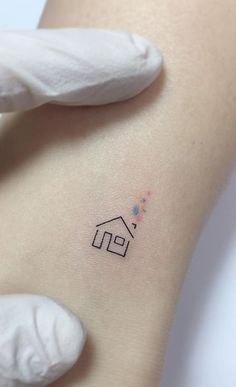 a small house tattoo on the back of a woman's left arm, with white gloves