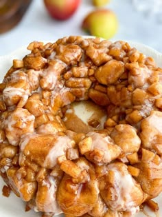 a donut covered in icing sitting on top of a white plate next to apples