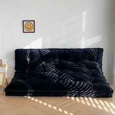 a black futon bed sitting on top of a hard wood floor next to a white wall