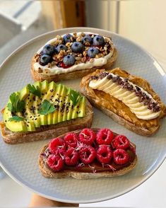 four slices of bread with fruit and nuts on them, sitting on a white plate