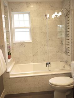 a white toilet sitting next to a bath tub under a window in a bathroom near a sink