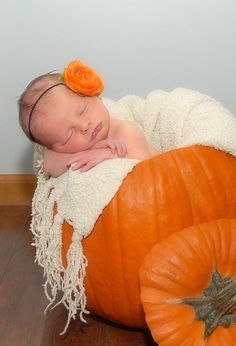 a baby sleeping on top of a giant pumpkin with a flower in it's hair