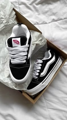 a pair of black and white vans shoes in a box on a bed with sheets