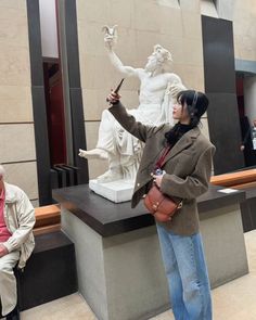 a woman standing in front of a statue with her hand up to the side and pointing at something