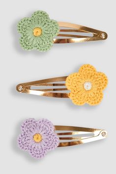 three crocheted flower hair clips are shown in three different colors, one yellow, one purple and one green