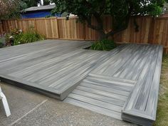 a large wooden deck in the middle of a yard with a tree and fence behind it