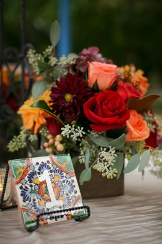 a table topped with a vase filled with red and orange flowers next to a card holder