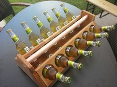 several bottles of beer are lined up in a wooden holder on an outdoor table with chairs