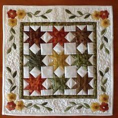 a quilted table topper with flowers and leaves on the border is displayed in front of a wooden surface