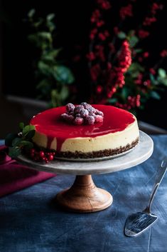 a cheesecake with raspberries on top sits on a cake plate next to a fork