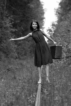 a woman in a dress is holding a suitcase and walking on a wooden path through the woods