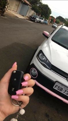 a person holding a cell phone in front of a white car with pink stripes on it