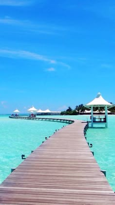 a wooden dock leading into the ocean with umbrellas on it's sides and blue skies in the background