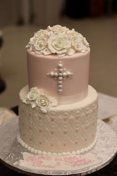 a three tiered cake decorated with white flowers and a cross on the top layer