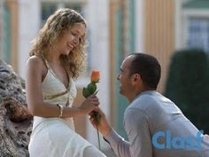 a man kneeling down next to a woman with a rose in her hand and holding it up