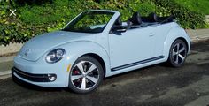 a light blue convertible car parked on the side of the road in front of some bushes