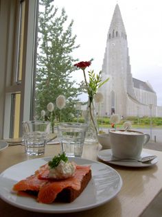 a plate with salmon and cream cheese on it sitting next to a window overlooking a church