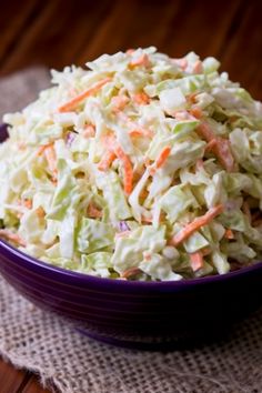 a purple bowl filled with coleslaw sitting on top of a wooden table next to a napkin