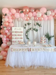 a table topped with balloons and cake next to a white wall covered in pink flowers