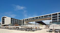 an empty beach with lounge chairs and umbrellas in front of a hotel on a sunny day