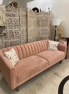 a pink velvet couch sitting in front of an ornate wooden paneled wall with decorative mirrors behind it