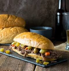 two sandwiches with meat, carrots and pickles on a black plate next to bread rolls