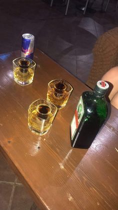 two empty glasses sitting on top of a wooden table next to a bottle and a can