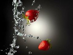 two strawberries splashing into water on a black background