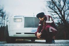 a man kneeling down in front of a white truck with the hood up and hands on his knees