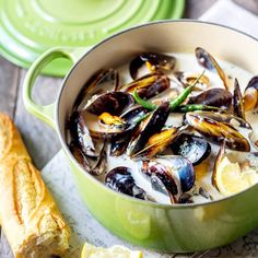 a green pot filled with mussels on top of a table next to bread