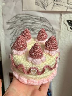 a small crocheted cake with pink and white frosting on top is being held up by someone's hand