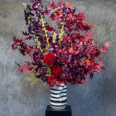 a vase filled with purple and red flowers on top of a black table next to a gray wall