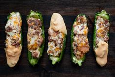 four stuffed peppers are lined up on a wooden surface, with sauce drizzled over them