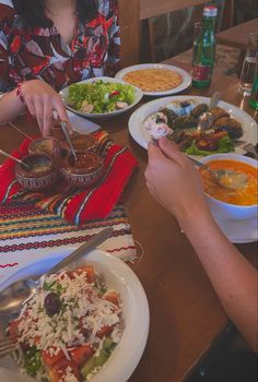 two people sitting at a table with plates of food in front of them and one person holding a fork