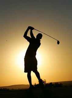 the silhouette of a man playing golf at sunset