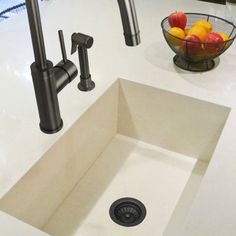 a white sink sitting under a kitchen faucet next to a bowl of fruit