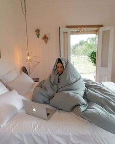 a woman wrapped up in a blanket on her bed with a laptop computer sitting on top of it